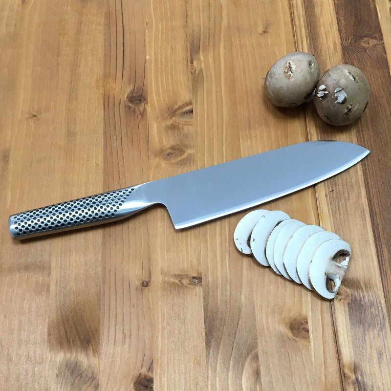 Cuchillo Global G-46 santoku sobre superficie de madera, perfil de hoja redondeada